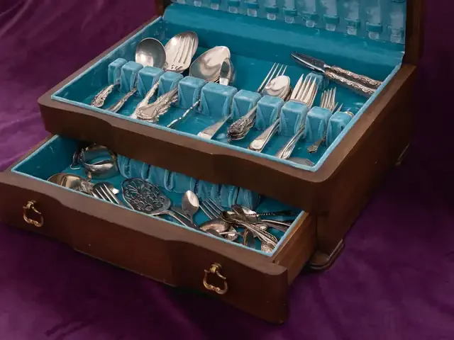 A wooden chest of silver flatware with its drawer open, on purple velvet