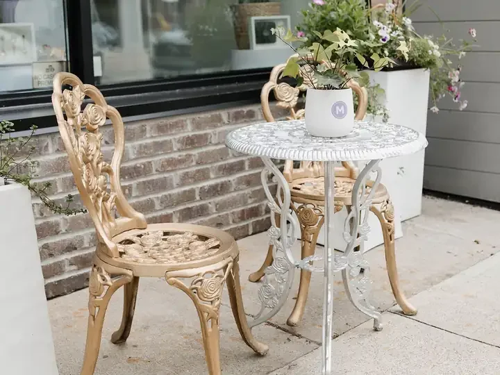 Gold bistro chairs and a white table outside the front window