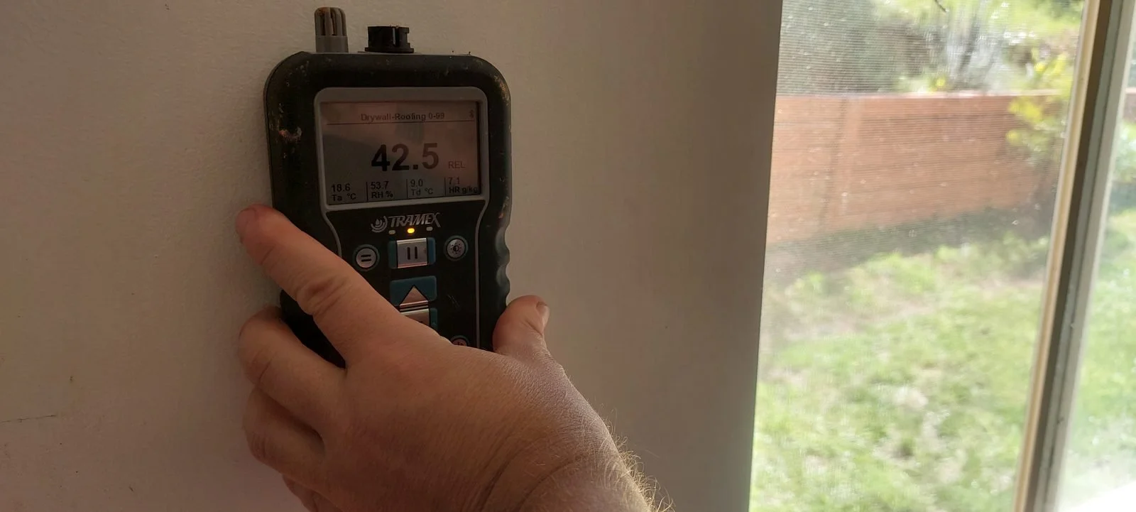 Joe Builds recording a moisture-indicator reading at a mapped wall location.