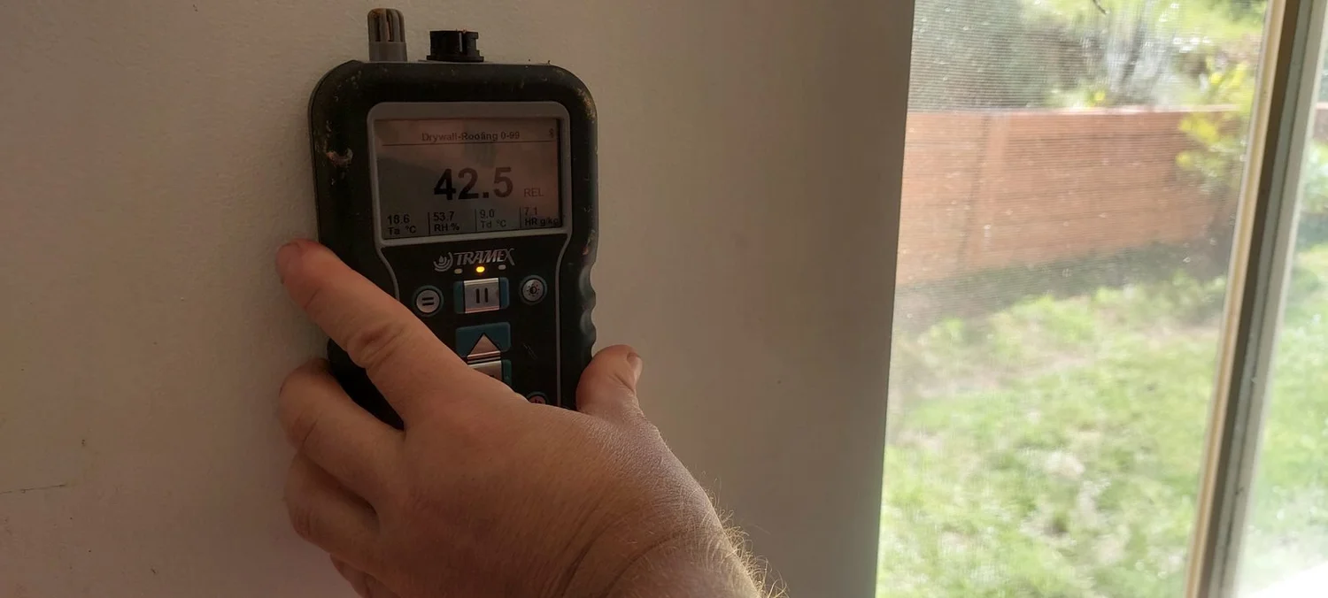 Joe Builds recording a moisture-indicator reading at a mapped wall location.