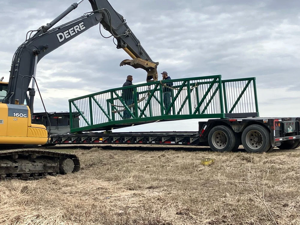 Green steel bridge being lifted onto a trailer by an excavator