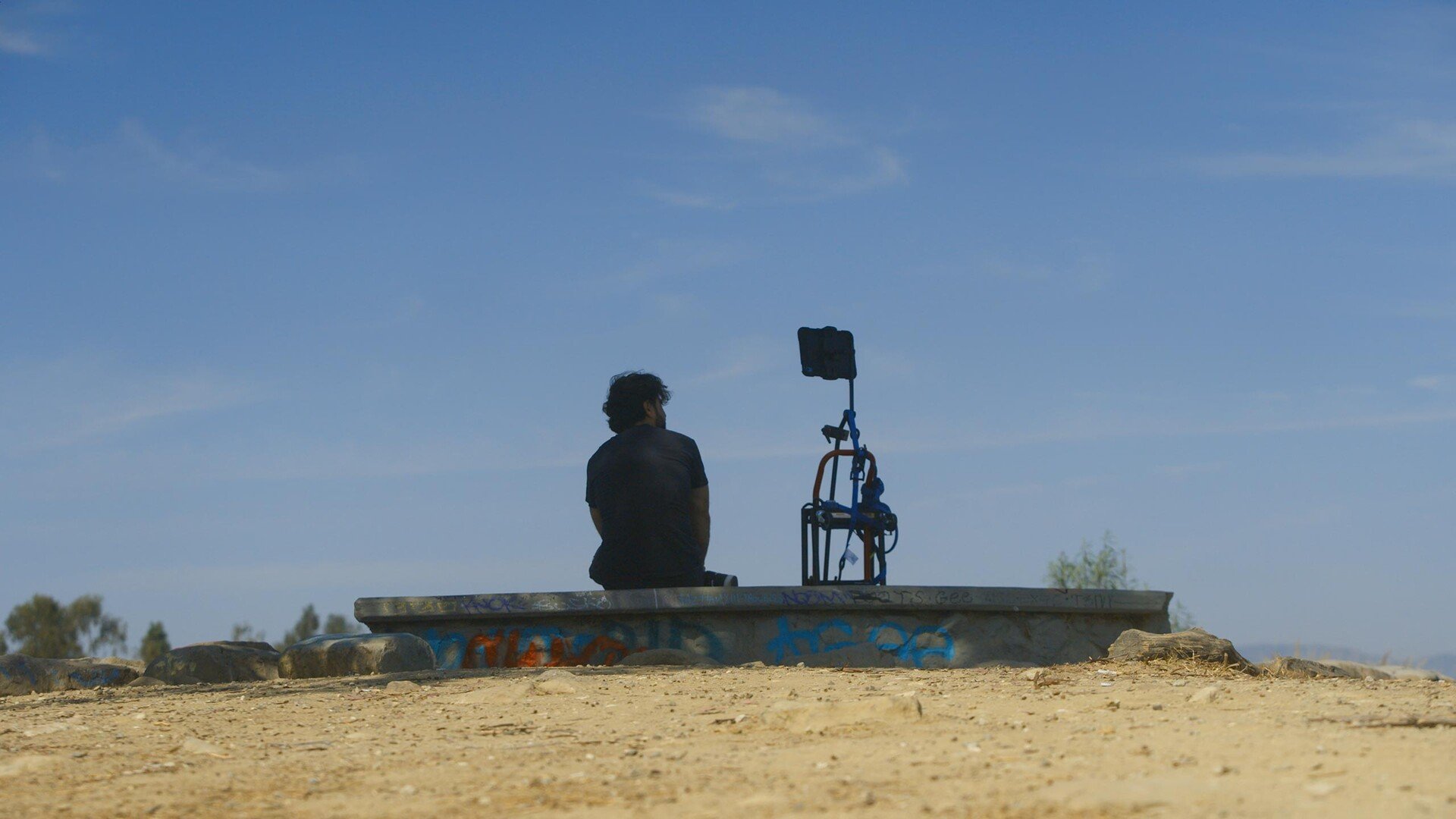 Deepfaking Sam Altman — person beside filming equipment beneath an open sky