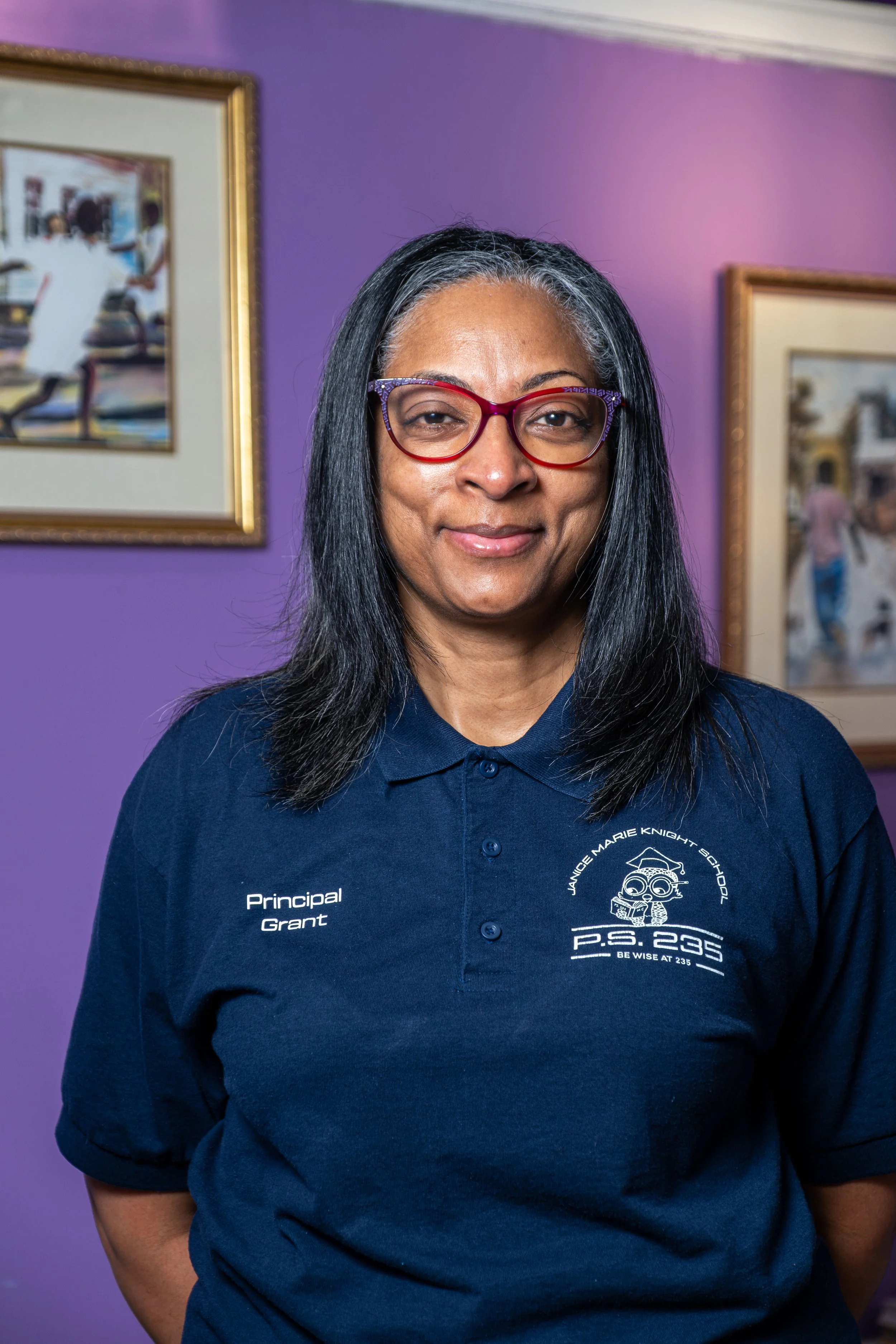 Principal wearing a navy blue polo shirt with school logo, standing and smiling