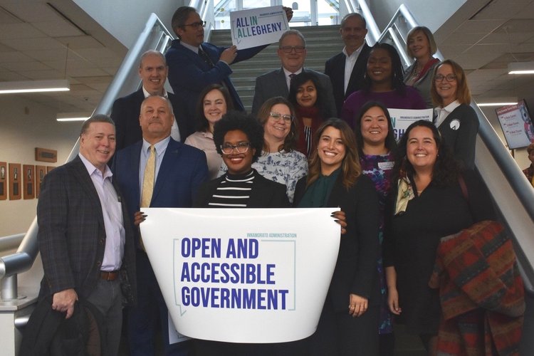 A group photo showing 20 elected officials holding a sign reading "Open and Accessible Government."