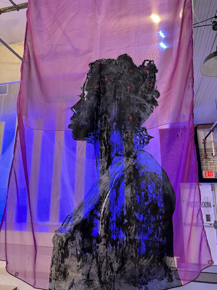 A silhouette of a woman is painted onto a purple piece of translucent fabric.