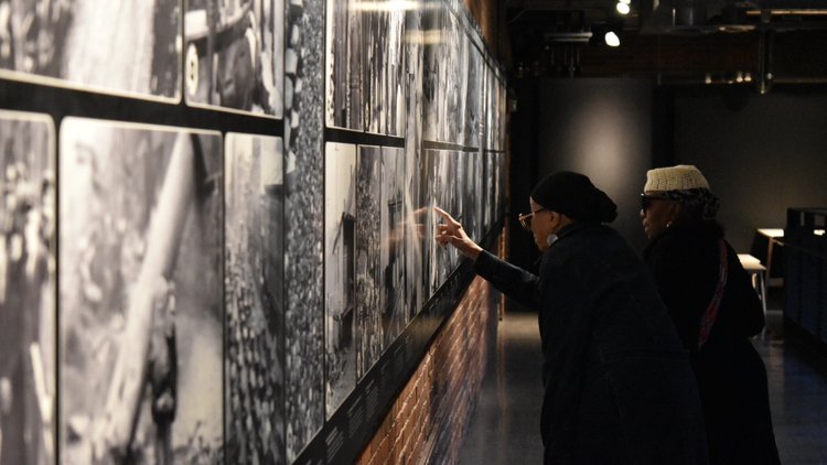 Two older African-American women point at a black-and-white photograph in an exhibit at the Heinz History Center.