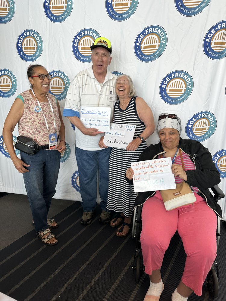 Four older adults holding signs that read: "Everyone inspired me to come to the National Senior Games," "I'm 78 years old and I feel fabulous!" & "Watching athletes compete at the National Senior Games makes me feel old & gold!" 