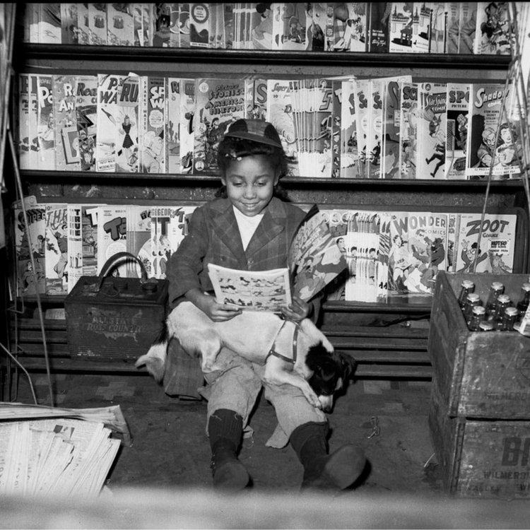 A black-and-white photo of a little girl reading a magazine.
