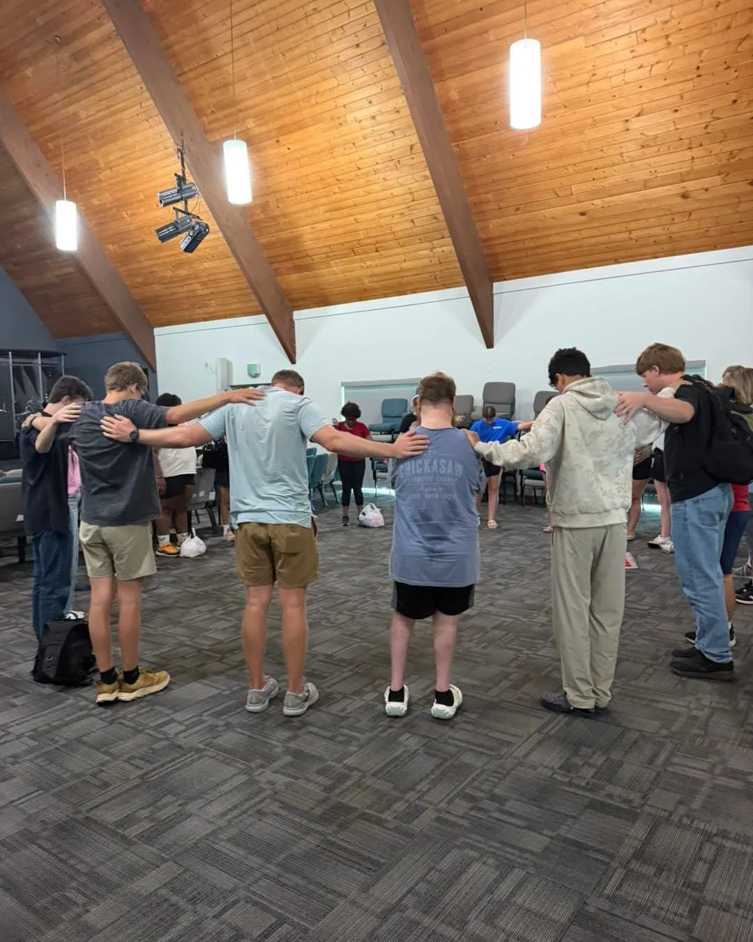 Young people gathered in a circle with their arms around one another inside a church hall.