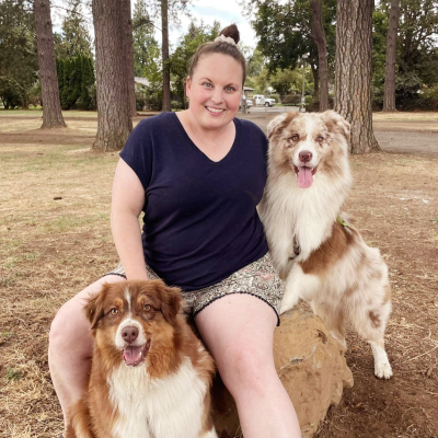 Image of employee Kim holding two dogs while kneeled and posing for photo