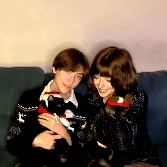Image of employee Tay and a friend posed for an image holding cats dressed in holiday clothes