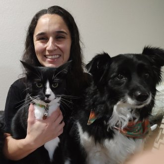 Posed image of Laura holding a black cat and two black and white dogs
