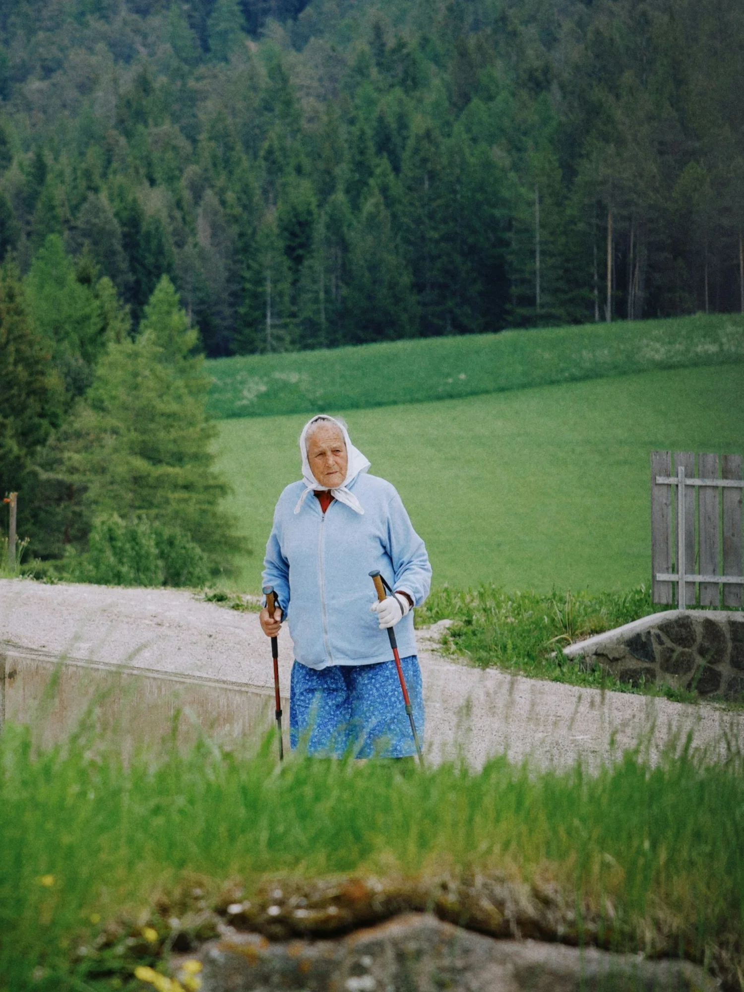 Older woman standing with two walking poles on a rural path.