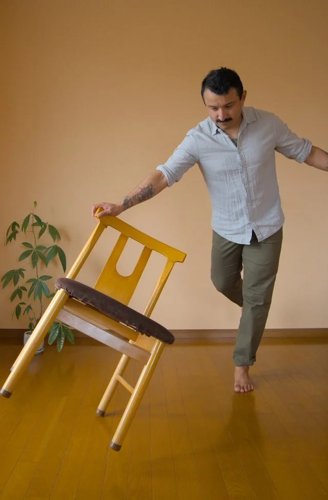 Man practices balance beside a sturdy chair in a controlled indoor setting