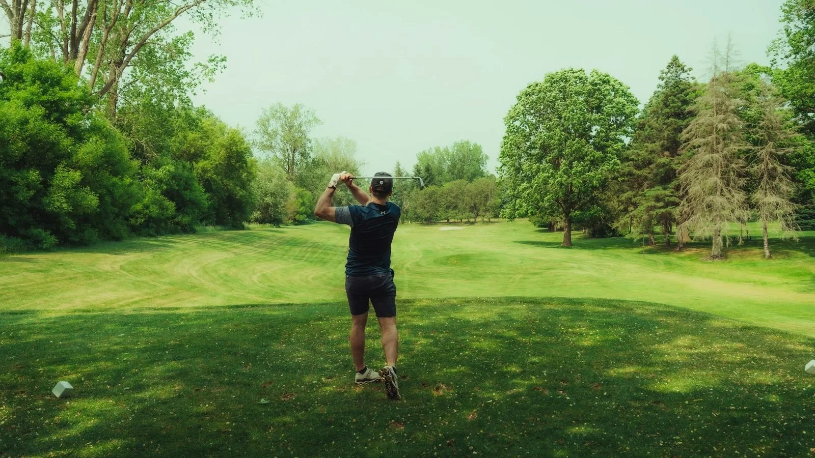 Golfer finishing an iron swing on a tree-lined fairway.