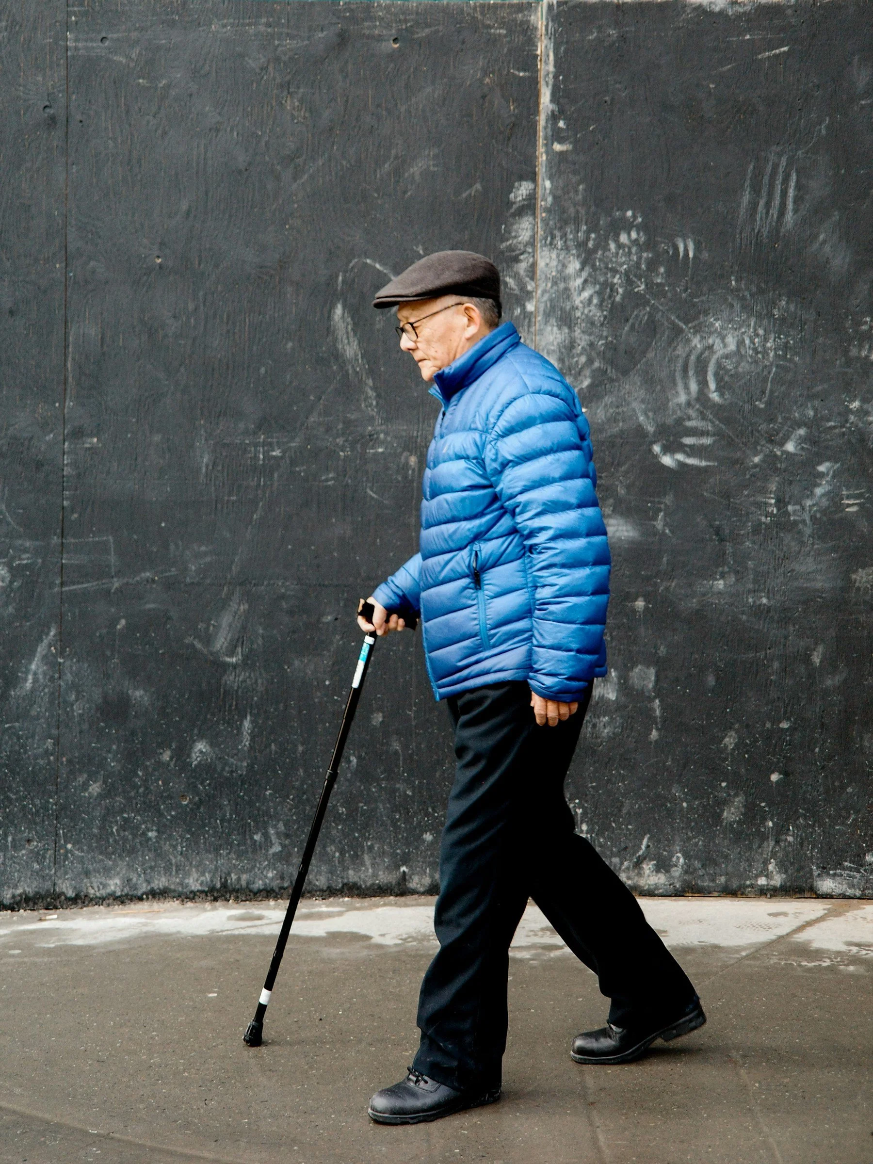 Older man in a blue jacket walking with a cane.