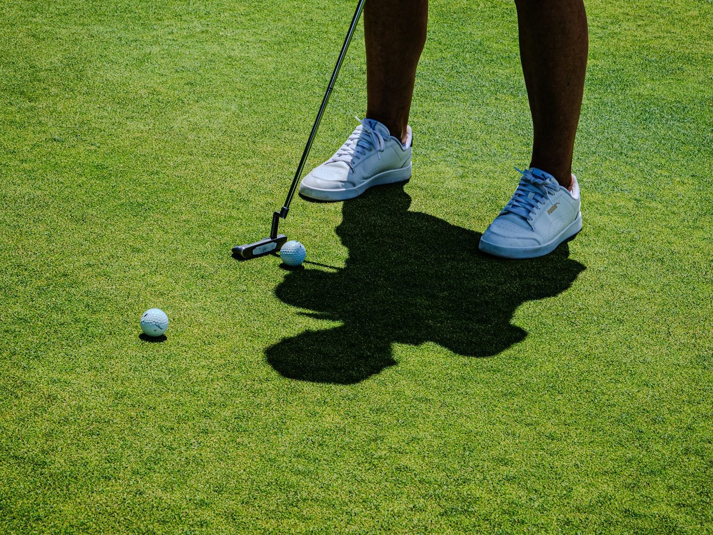 Golfer practicing a putt on a sunlit green.