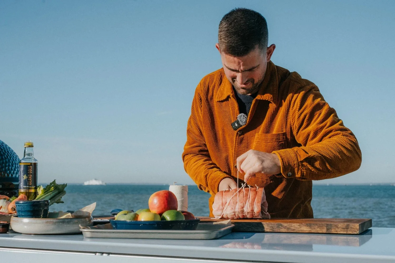 Chef Robert Thompson preparing meat on the outdoor kitchen counter, the sea behind him