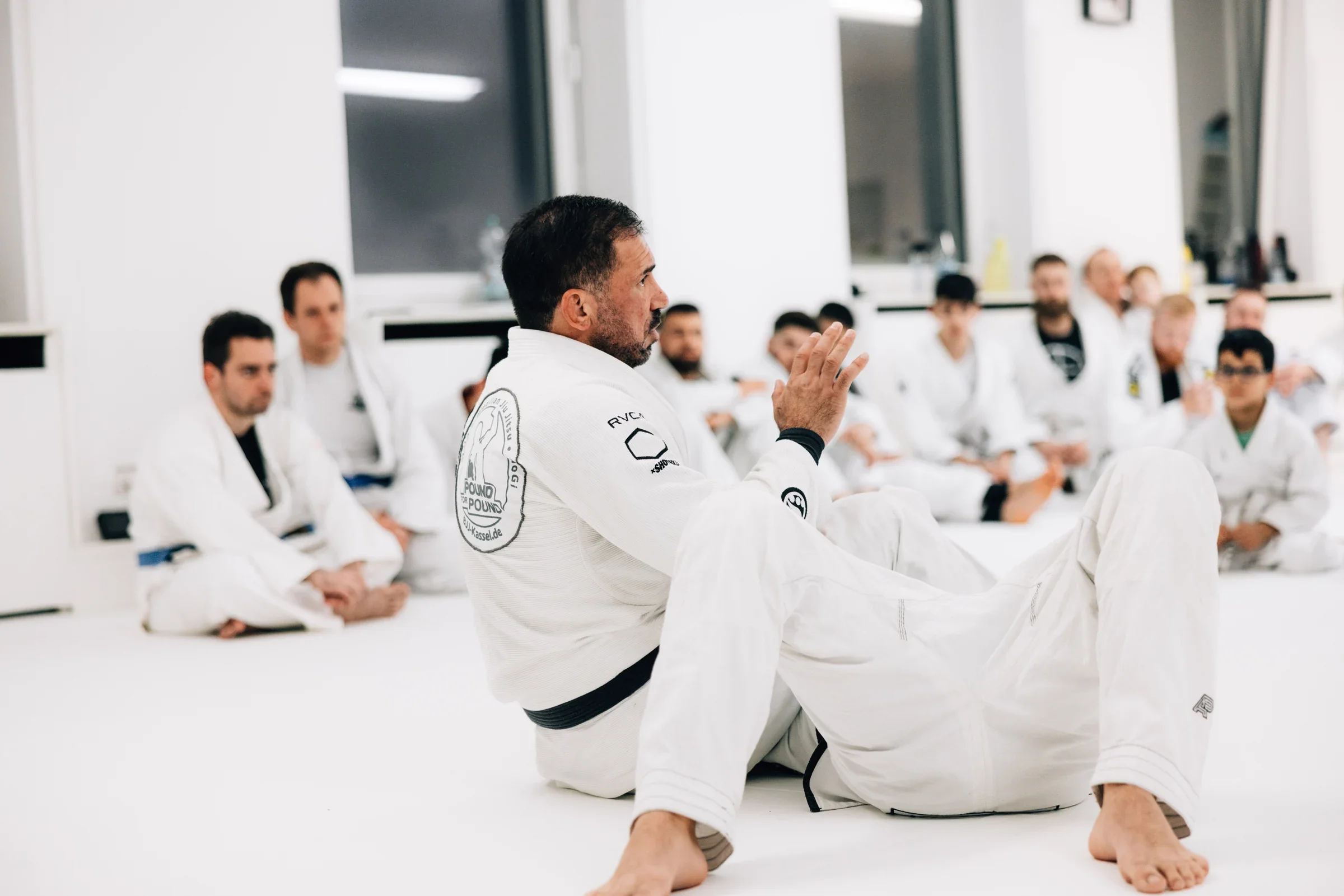 Eine sitzende Trainingsgruppe verfolgt eine Erklärung mit Handgeste im PFP-Gym