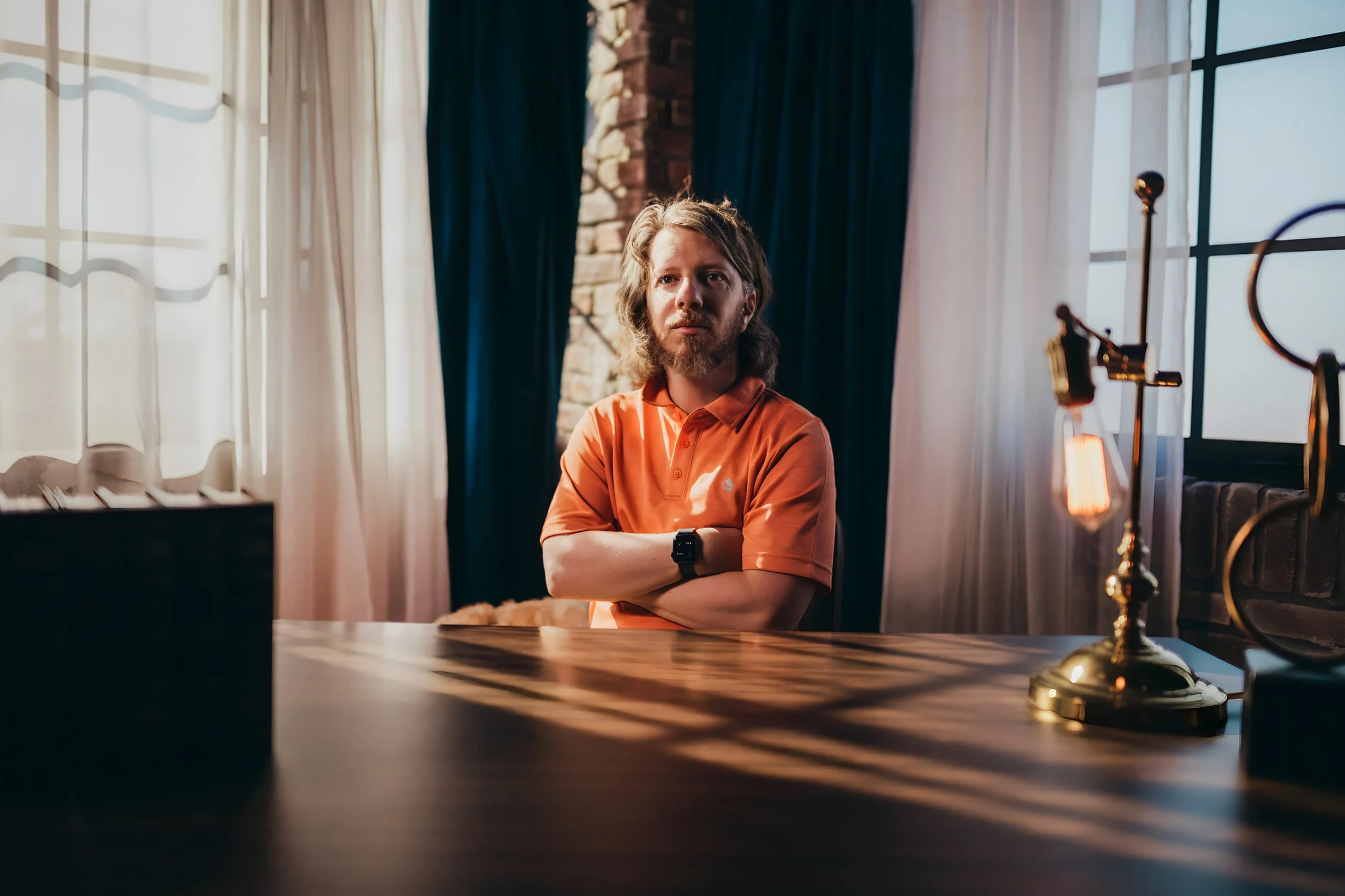 Brendan Oakes seated at a wooden desk with arms crossed.