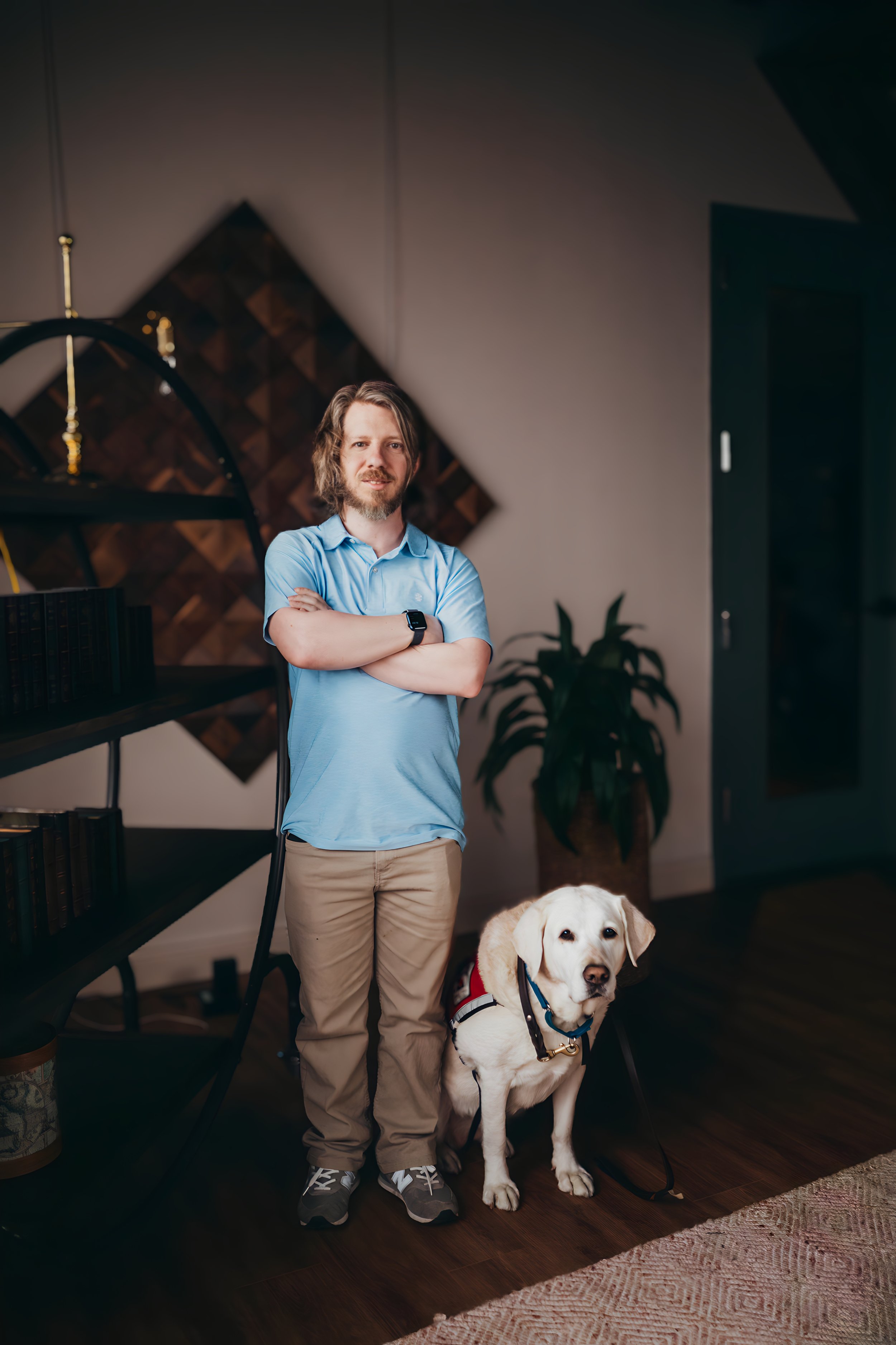 Brendan Oakes standing beside his yellow Labrador service dog wearing a red Service Dogs of Virginia vest.