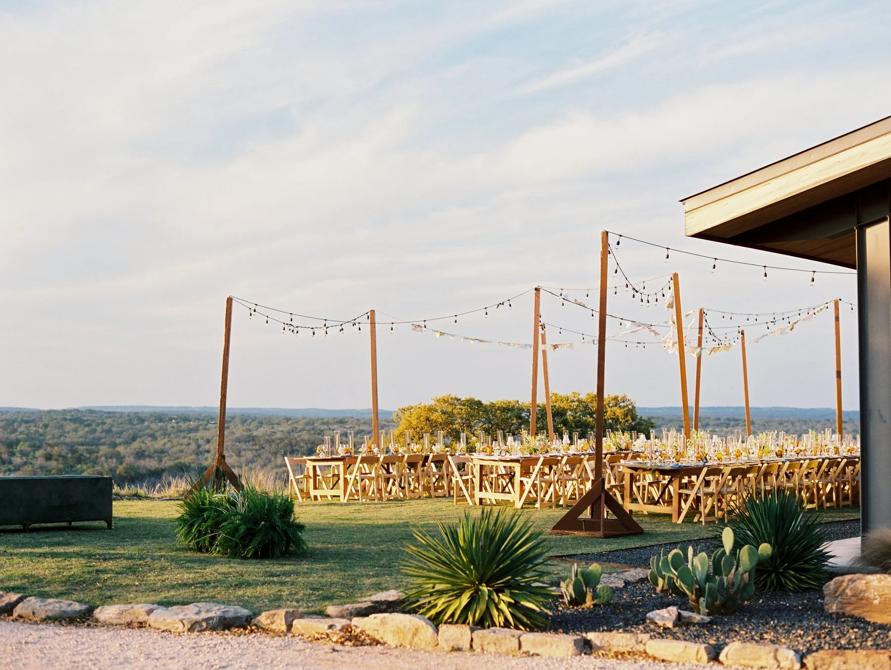 Outdoor wedding tables beneath string lights with a Hill Country view.