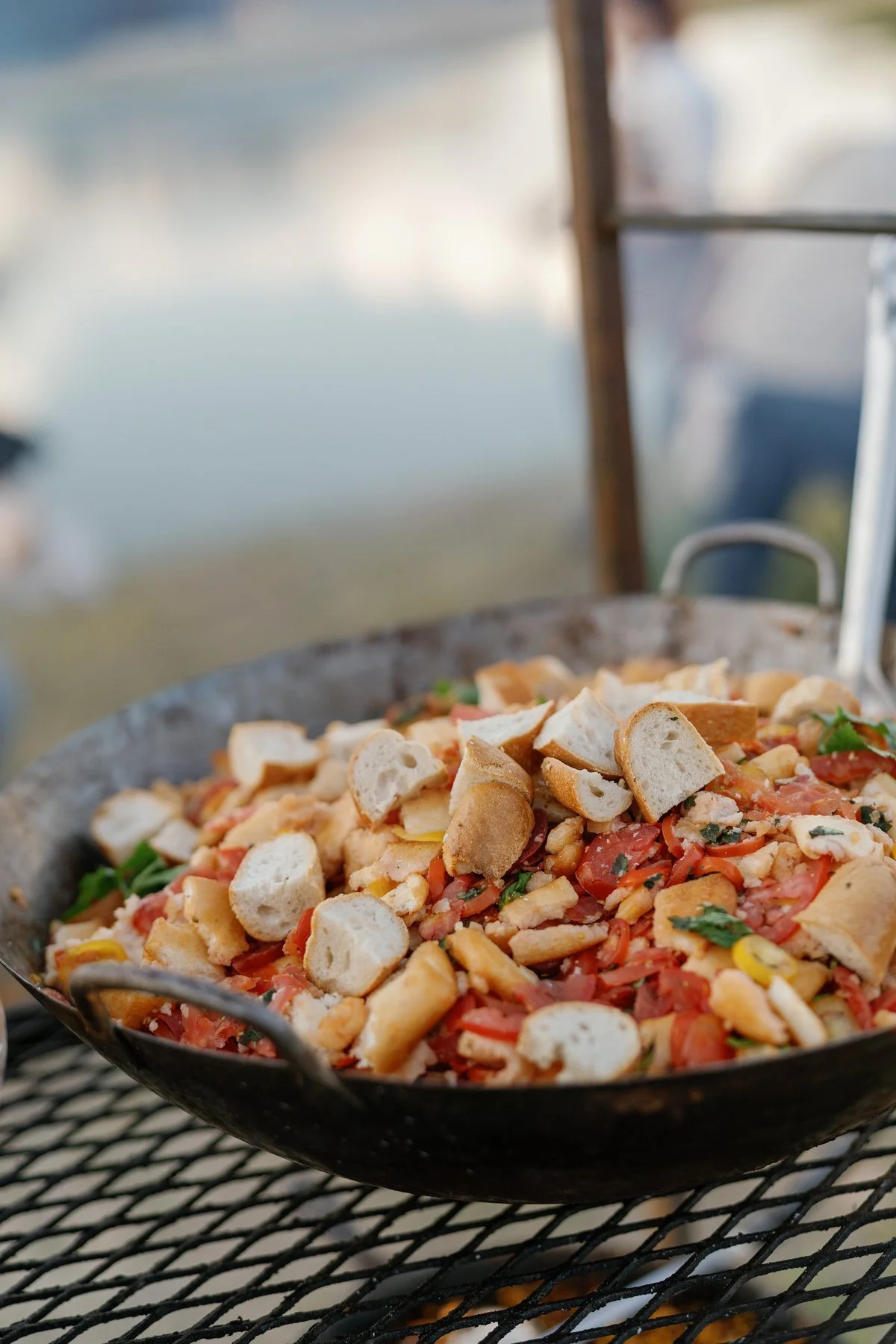 A large serving pan of colorful food and bread beside the live-fire setup.