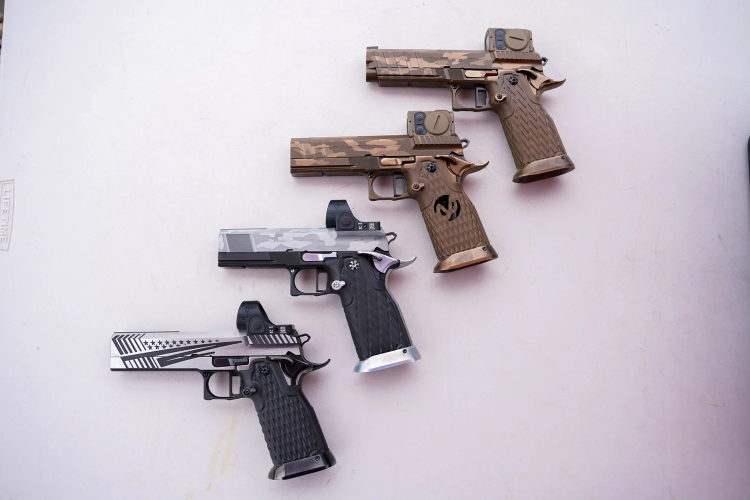 Four competition pistols with red dot optics laid out on a table