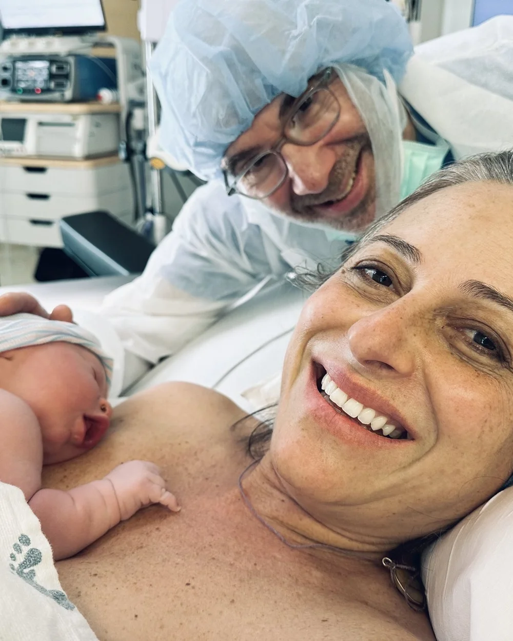 Jess smiling with her newborn son on her chest and her husband beside her