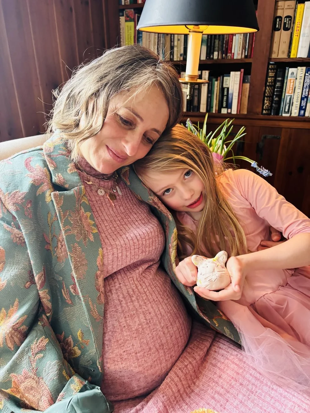 Jess, pregnant, cuddled up on the couch with a little girl holding a clay mouse