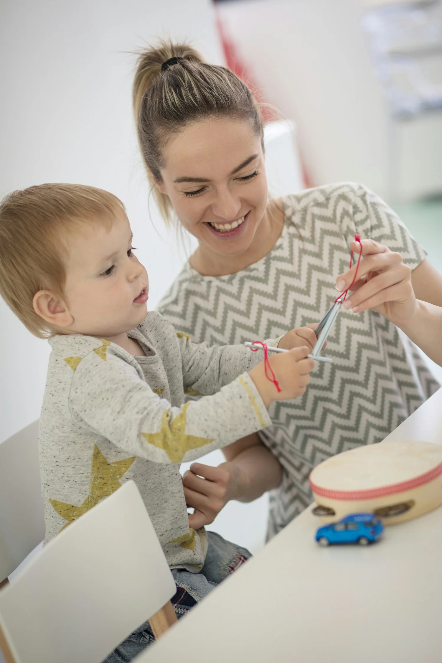 A caregiver helping a toddler with a fine-motor activity at a table