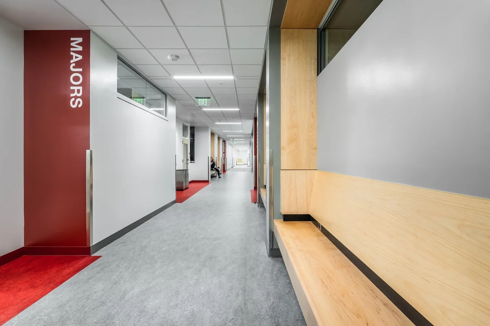 Quiet corridor with a long timber bench and red wayfinding column.