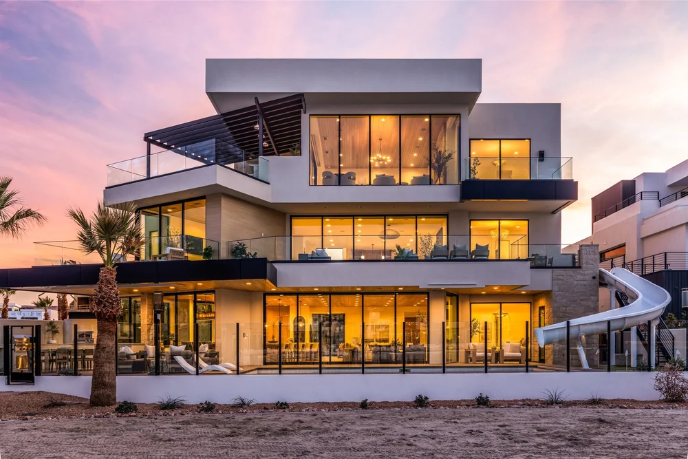 Modern multi-level home with illuminated windows beneath a pink twilight sky