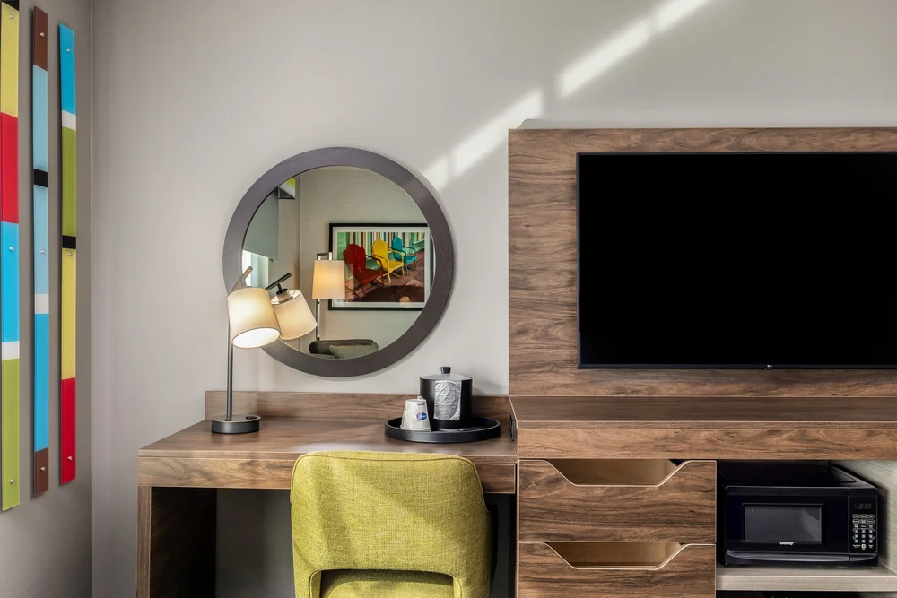 Guest-room desk with a circular mirror, lime-green chair and wood cabinetry.