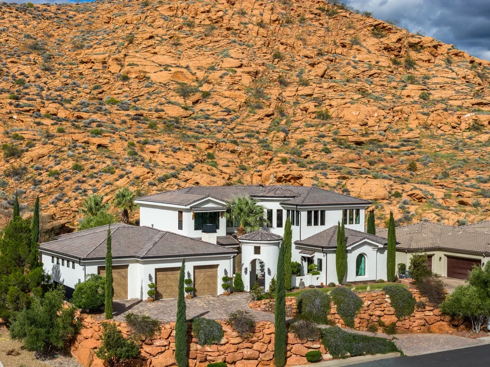 Aerial view of a white house beneath a red-rock hillside
