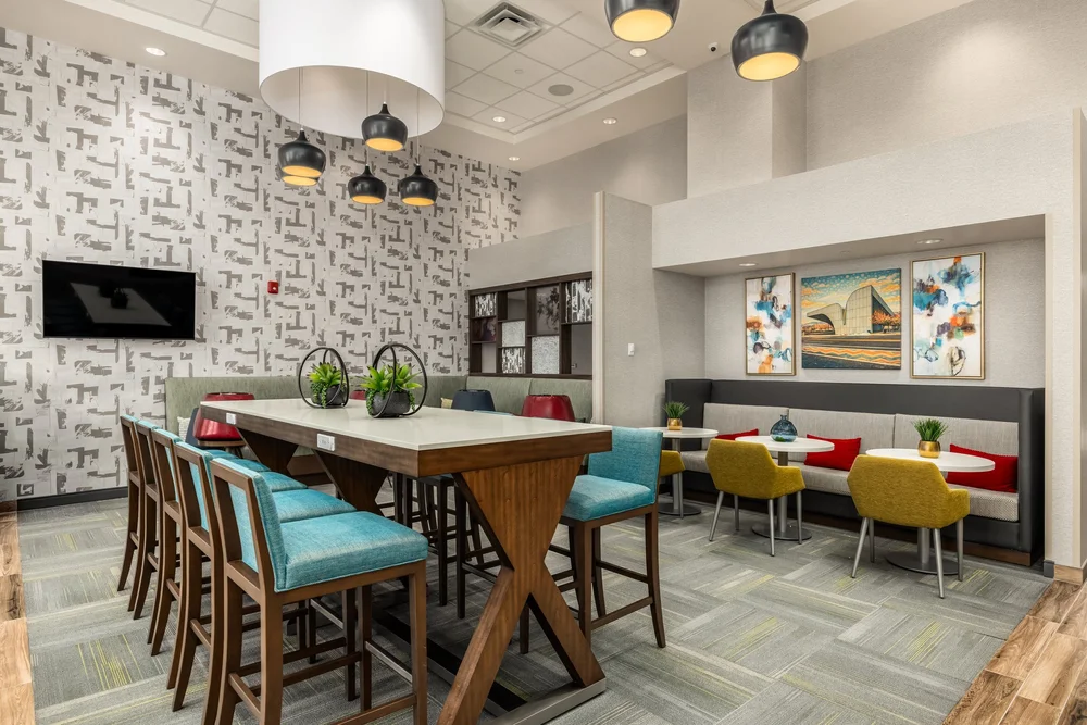 Hotel dining lounge with pendant lights, a communal table and colorful upholstered seating.