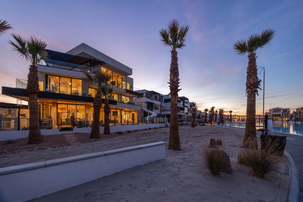Angled view of a glowing modern home and palm-lined path at twilight