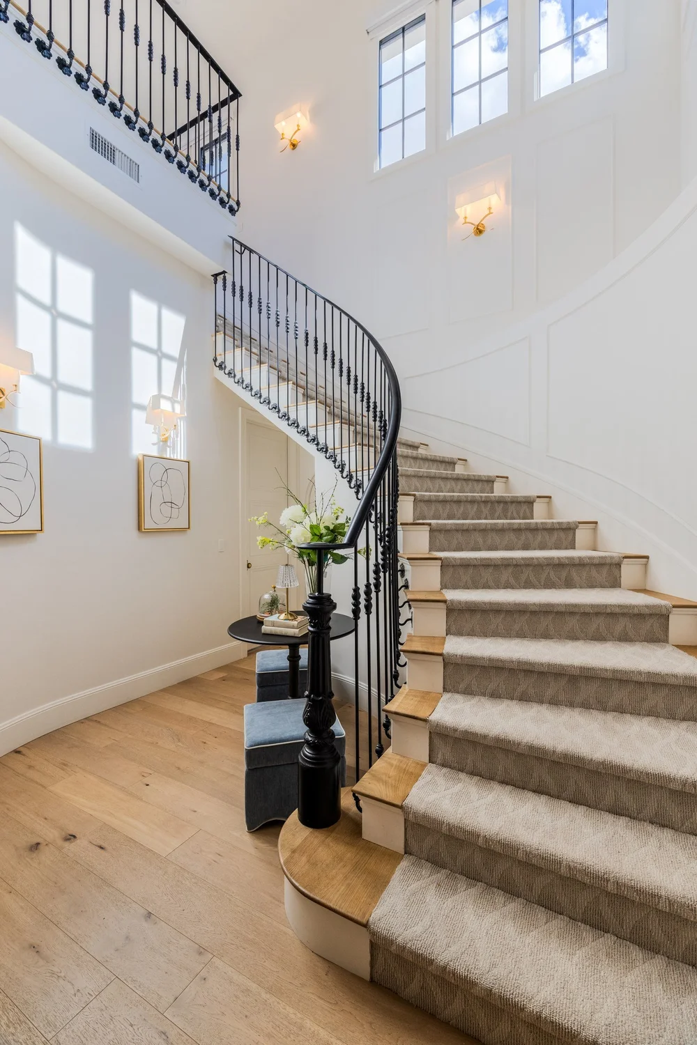 Sunlit curved staircase with black iron railing and tall windows