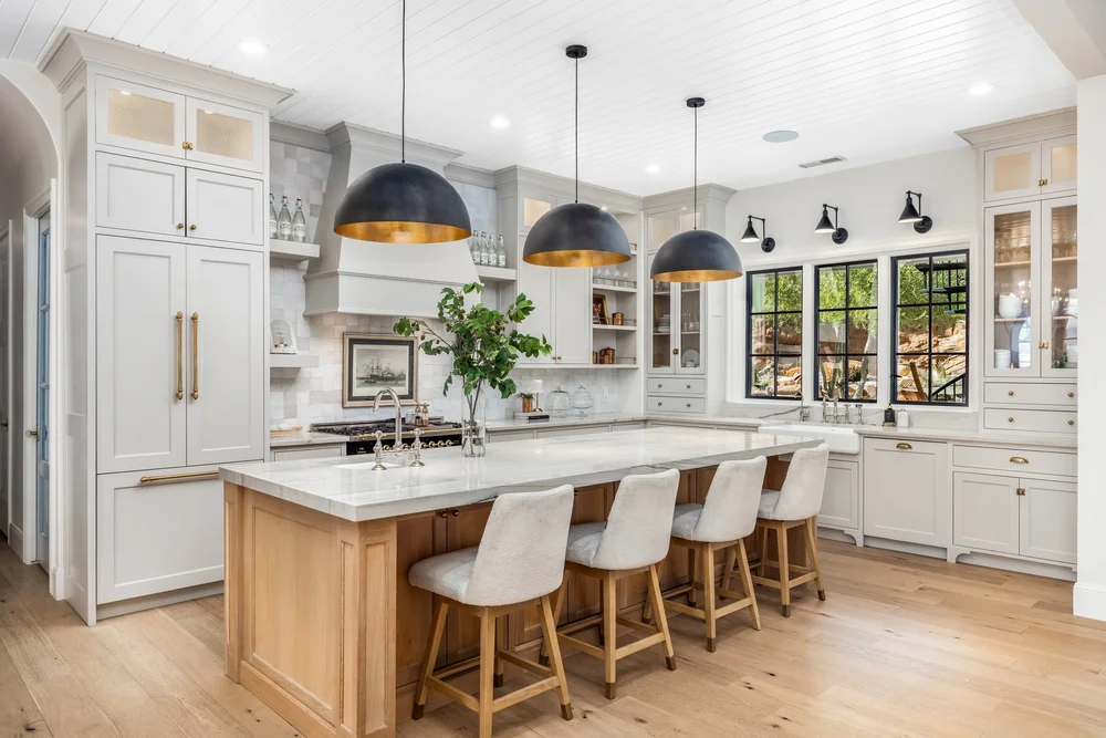 Bright kitchen with a wood island, white cabinetry and black pendant lights