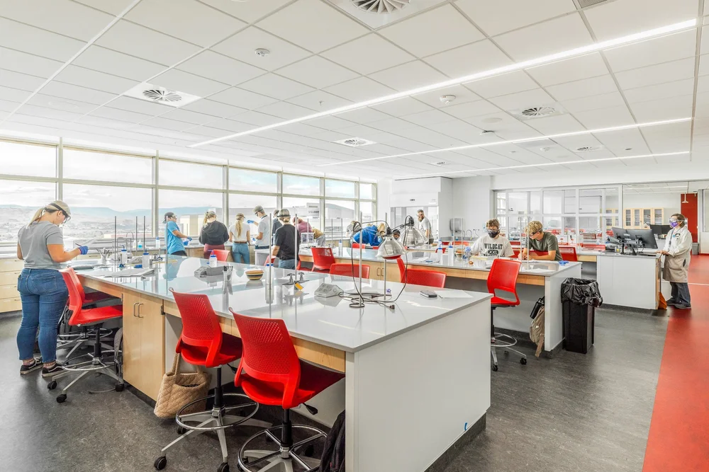 Bright laboratory interior with white workbenches, red chairs and occupants at work.