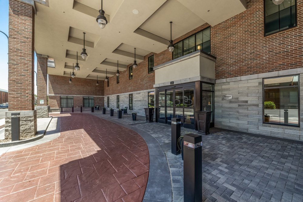 Covered hotel arrival with brick walls, stone accents, glass entry doors and geometric paving.