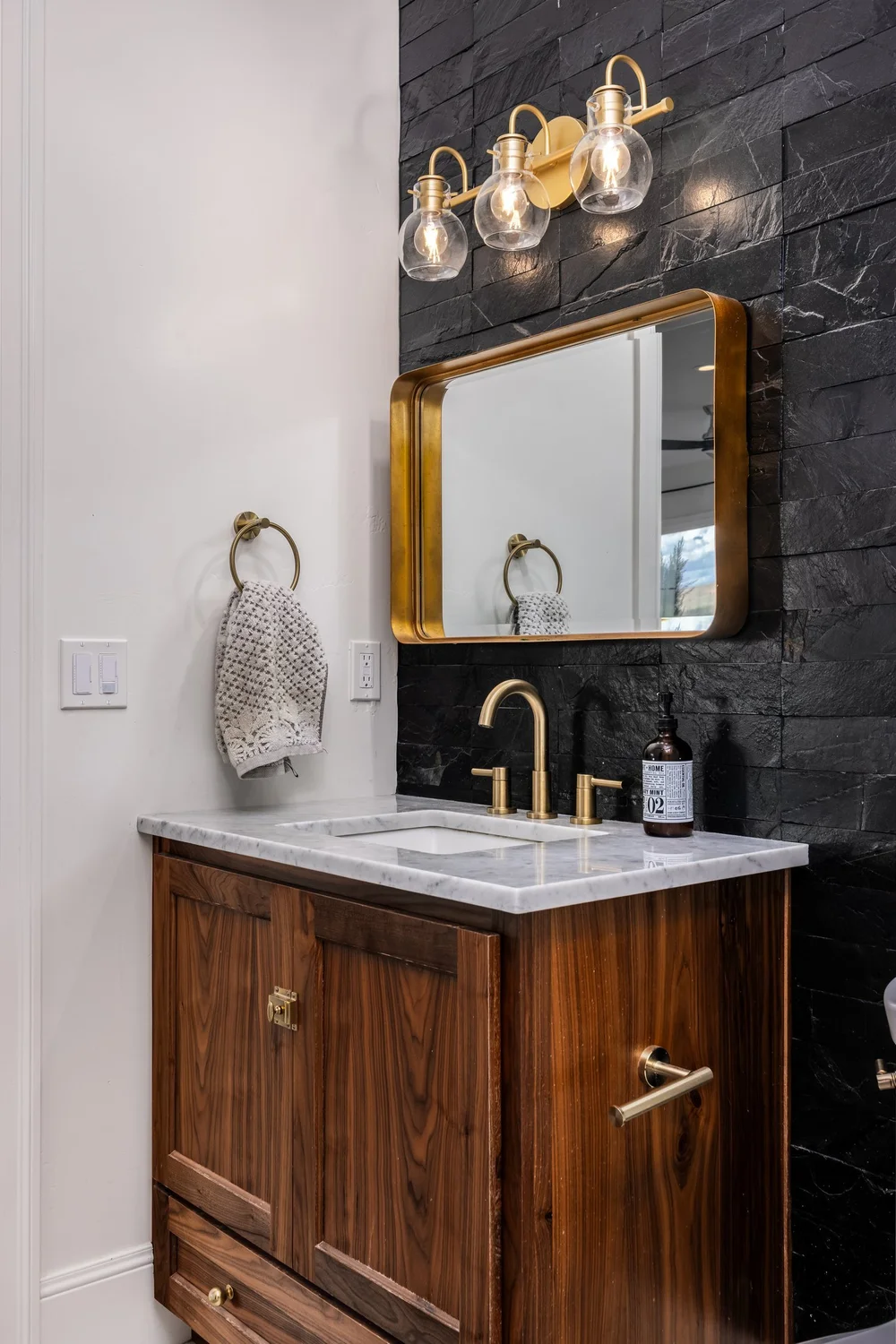 Powder room with a wood vanity, brass mirror and dark accent wall