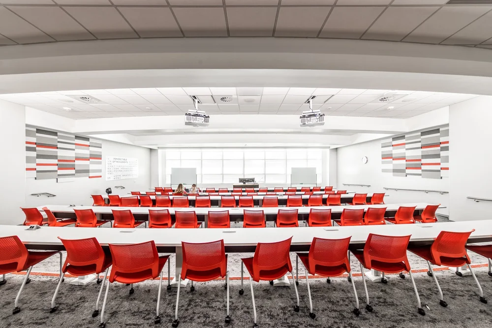 Tiered lecture room with red seating and broad windows at the front.