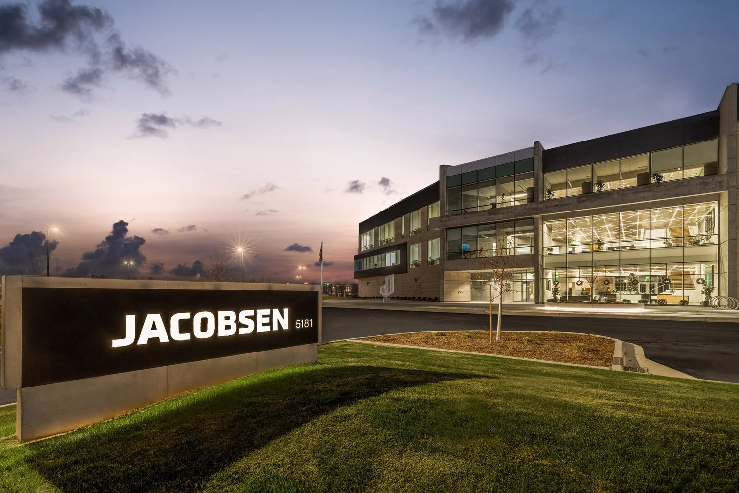 Illuminated Jacobsen sign and glass-fronted headquarters after sunset.