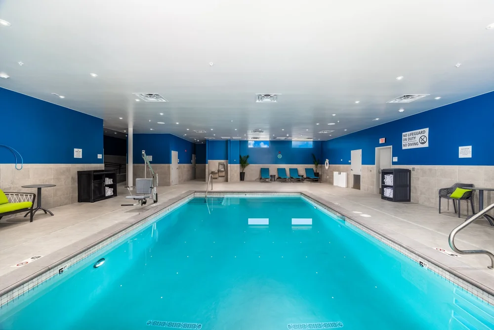 Indoor hotel pool framed by blue walls and a row of lounge chairs.