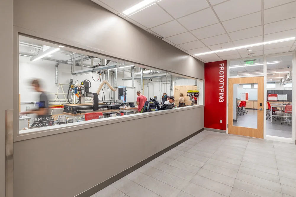 Glass-walled prototyping workshop beside a corridor with red wayfinding signage.