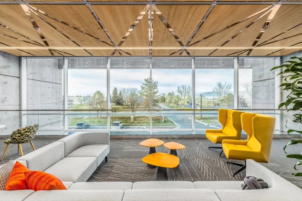 Daylit workplace lounge with yellow chairs beside floor-to-ceiling windows.
