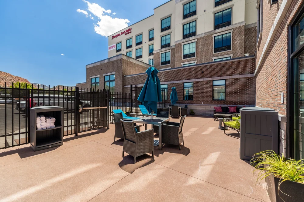 Outdoor hotel patio with seating, closed umbrellas and the brick hotel facade rising behind.