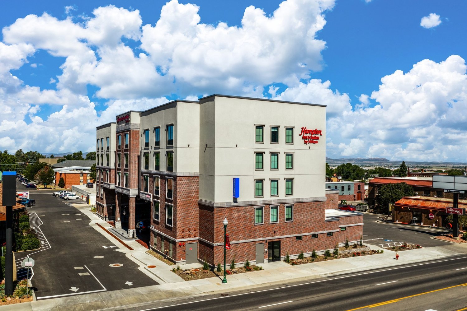 Hampton Inn & Suites in Cedar City, photographed from an elevated corner view beneath bright clouds.