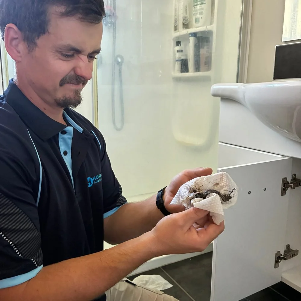 Isaac grimacing at a hair clog he has just removed from under a bathroom sink